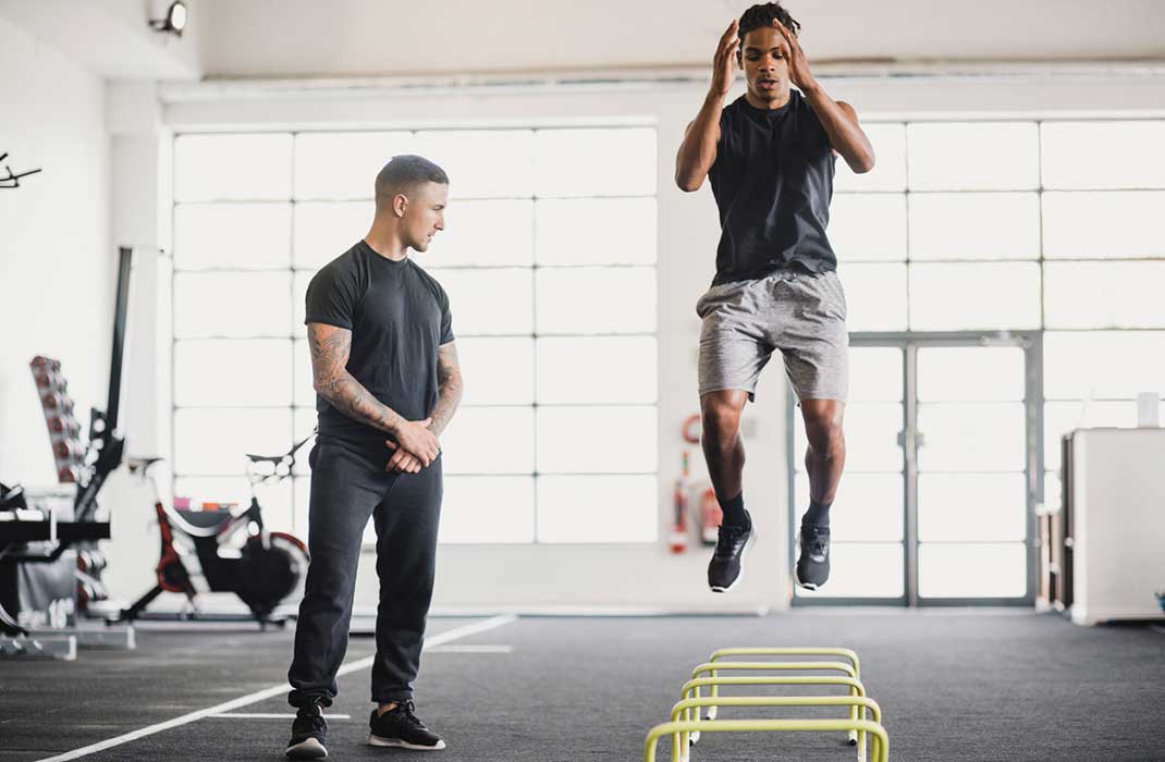 athletic trainer with client performing jumping exercise in gym
