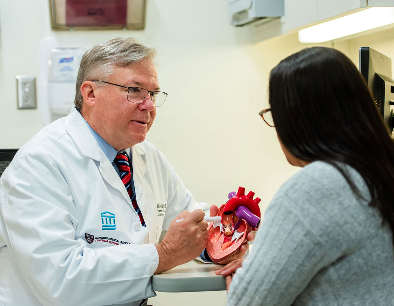 male provider holding a 3D model of the human heart while talking to female patient