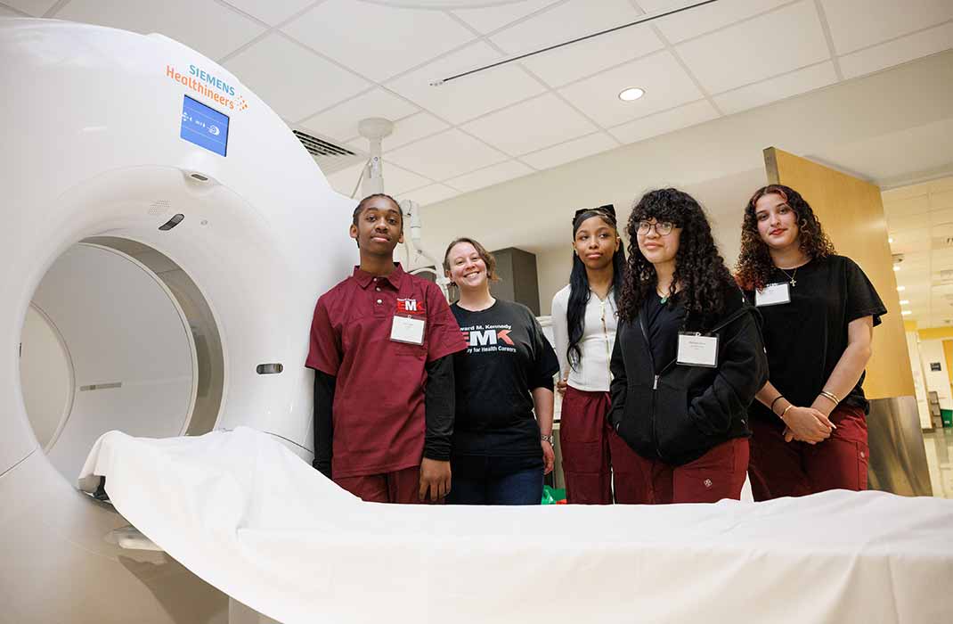 Five students are standing next to an MRI machine