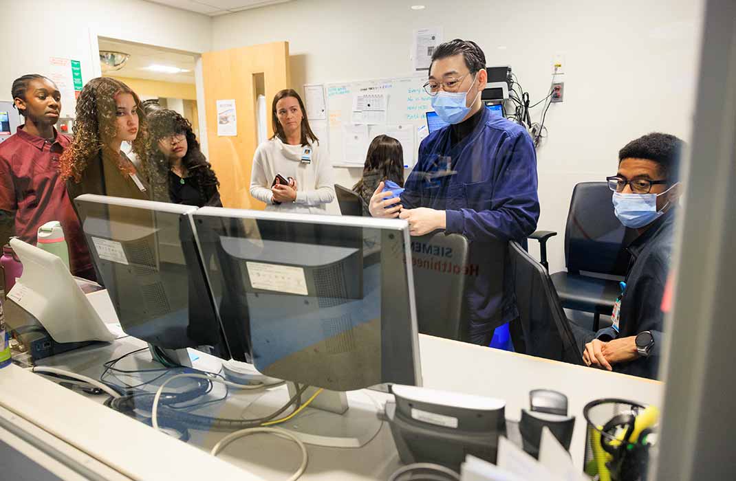 A group of six people standing at a medical workstation and looking at monitors
