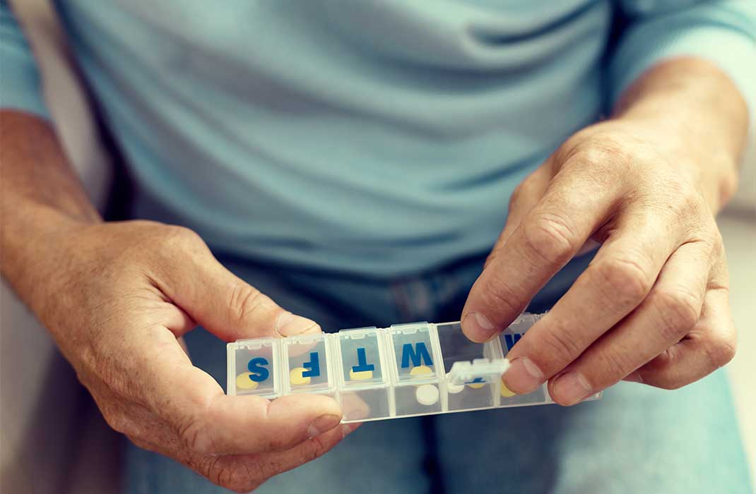 A man opens a compartment of his daily pill organizer.
