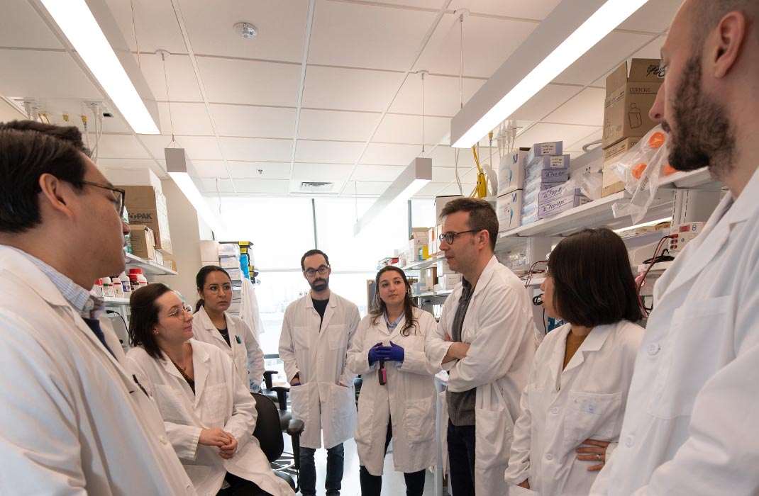 A group of 8 researchers in lab coats standing and having a discussion