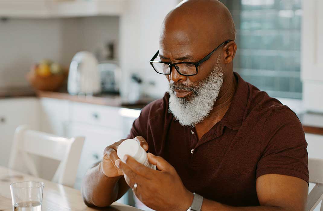 An older man reading a bottle of pills in his kitchen.