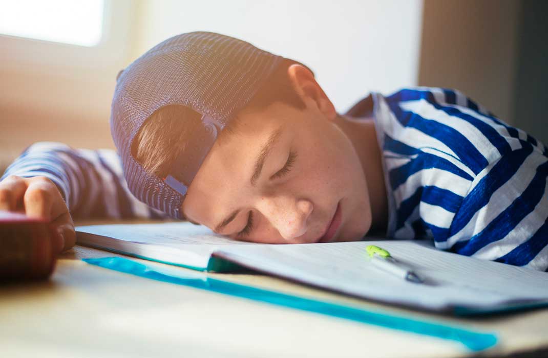 A male teen wearing a cap backwards is asleep on his textbooks