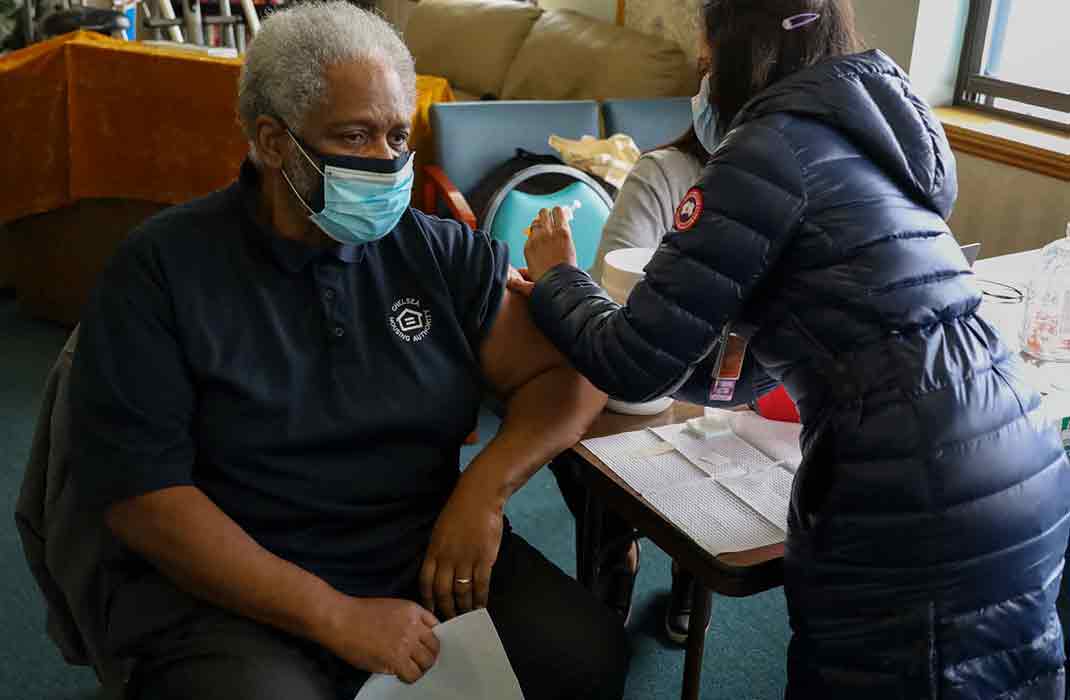 Elderly masked individual receiving a vaccine administered by a healthcare worker