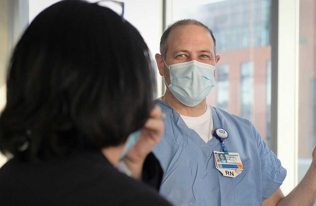 A nurse in scrubs talks to a patient.