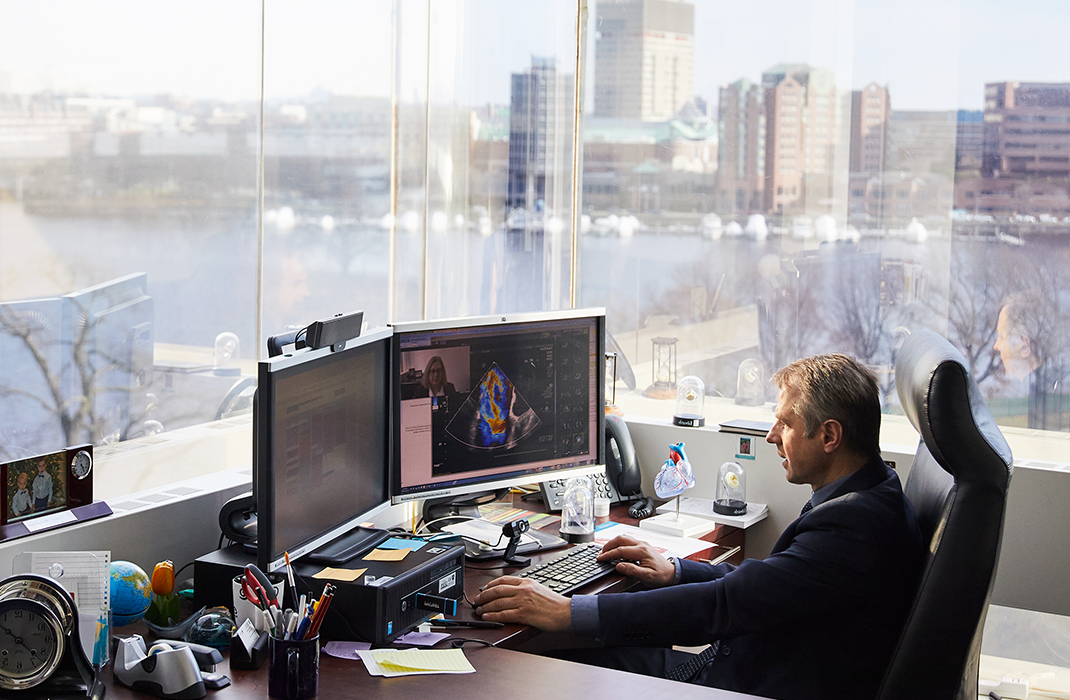 doctor in office at computer with view of Boston skyline out windows 