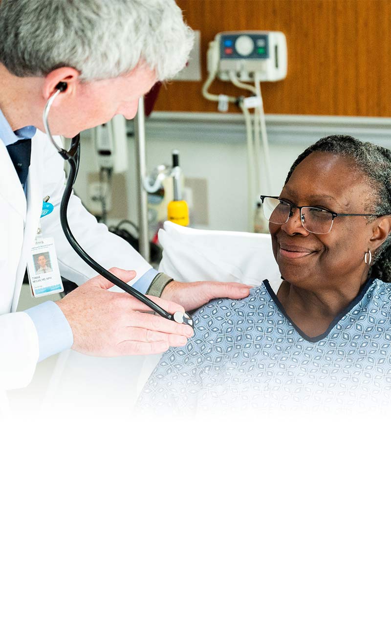 male provider with female patient at bedside using stethoscope
