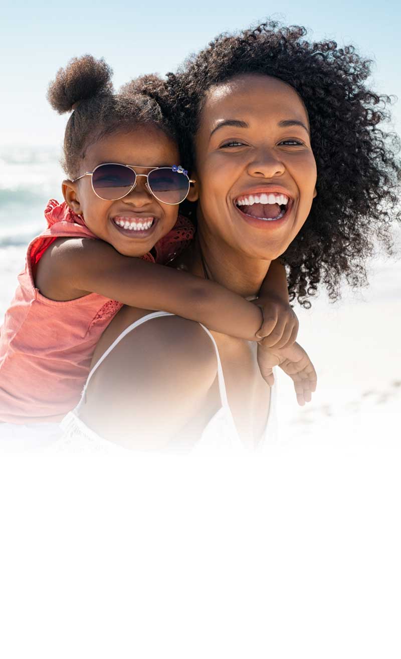 mother with young daughter on her back smiling at the beach