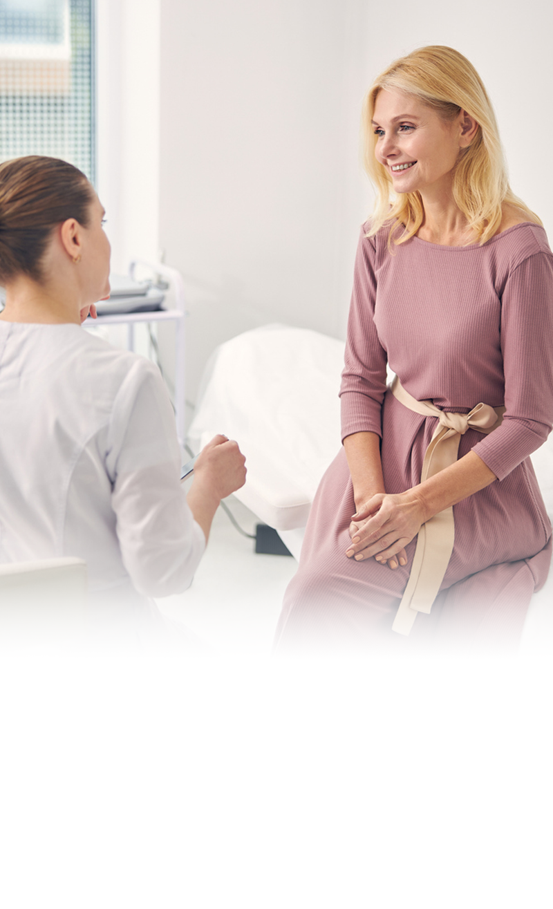 A patient sits on an exam table while speaking with a healthcare professional. 