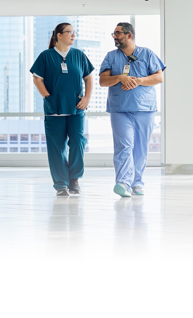 two clinicians in scrubs walking down hallway conversing