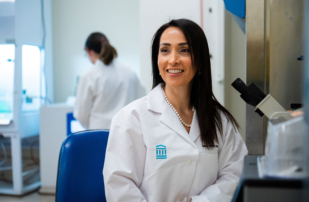 A woman in a white coat near a microscope in a lab setting