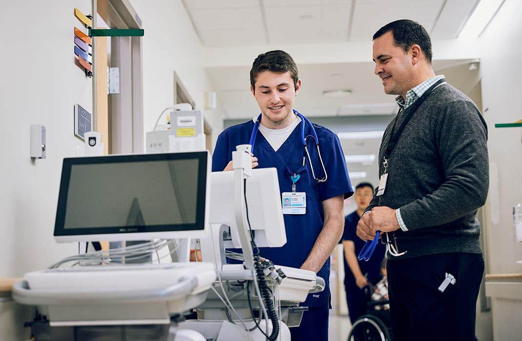 Two male clinicians standing next to monitor in hallway