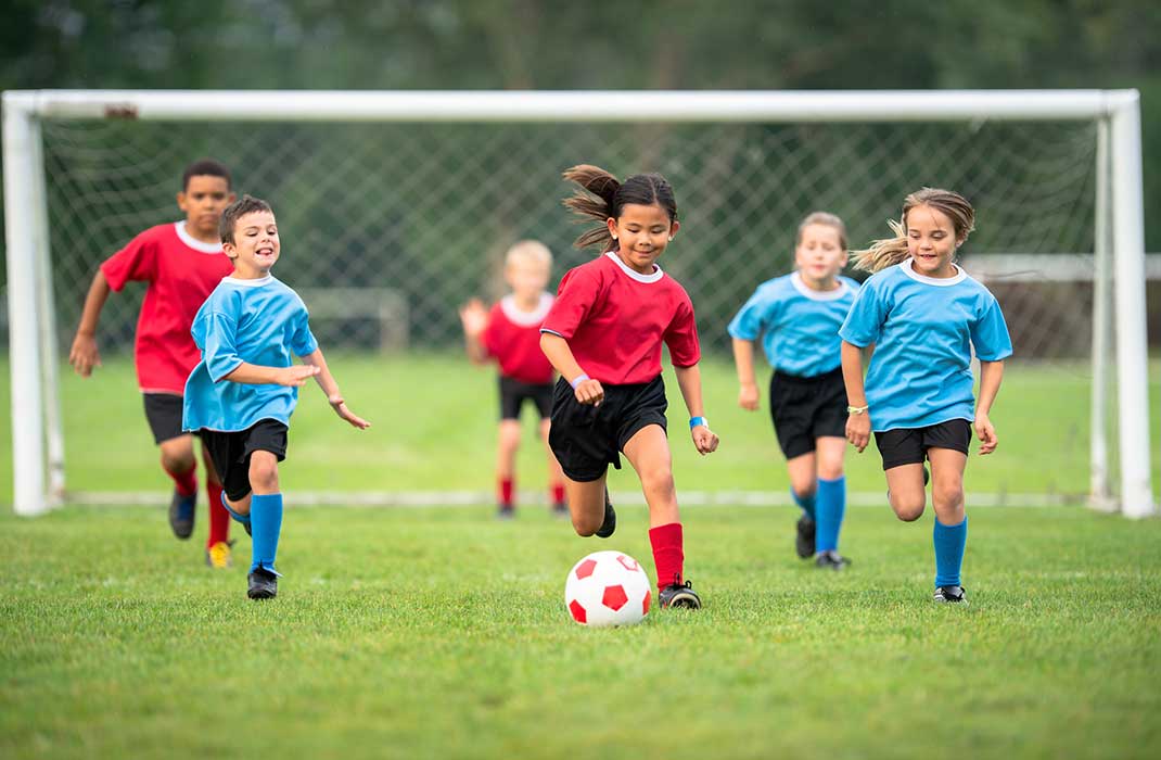 Children in red and blue jerseys playing soccer.