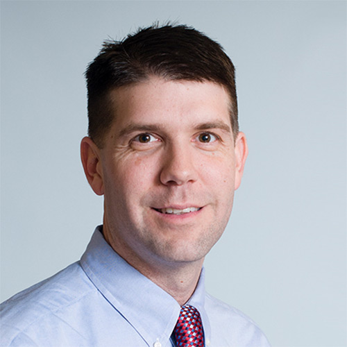 Headshot of an adult man wearing a light blue dress shirt and patterned tie.