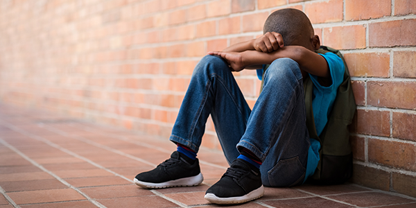 child sitting against a wall with head in his legs