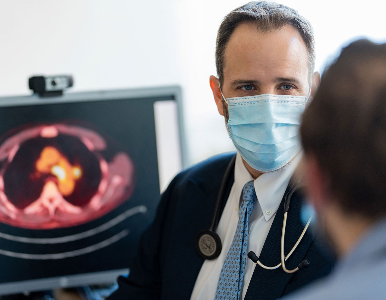 طبيب يرتدي كمامة يتحدث مع مريض، وتظهر صورة أشعة على شاشة الكمبيوتر