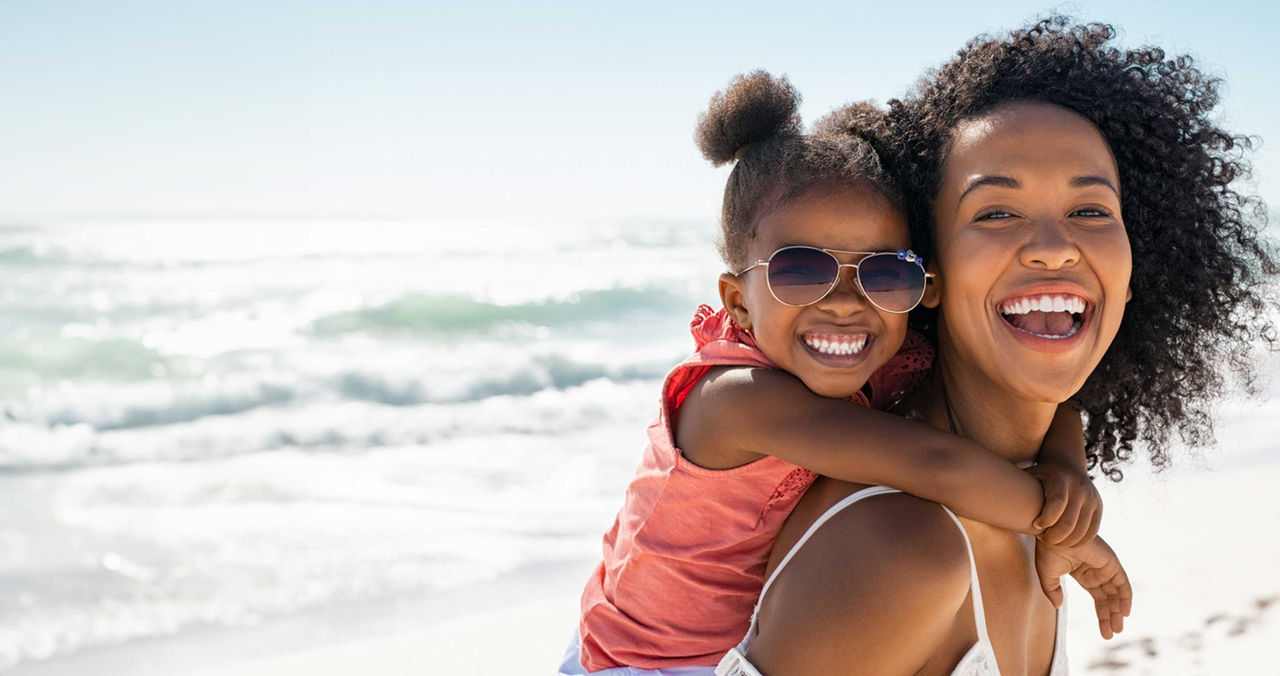mother with young daughter on her back smiling at the beach