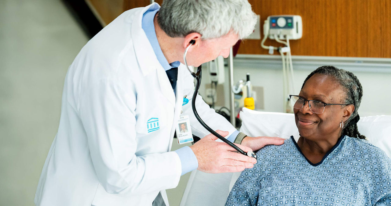 male provider with female patient at bedside using stethoscope
