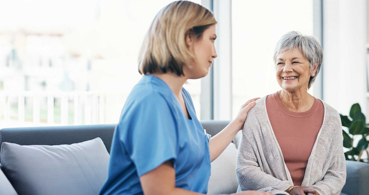 female provider with hand on shoulder of smiling older female patient