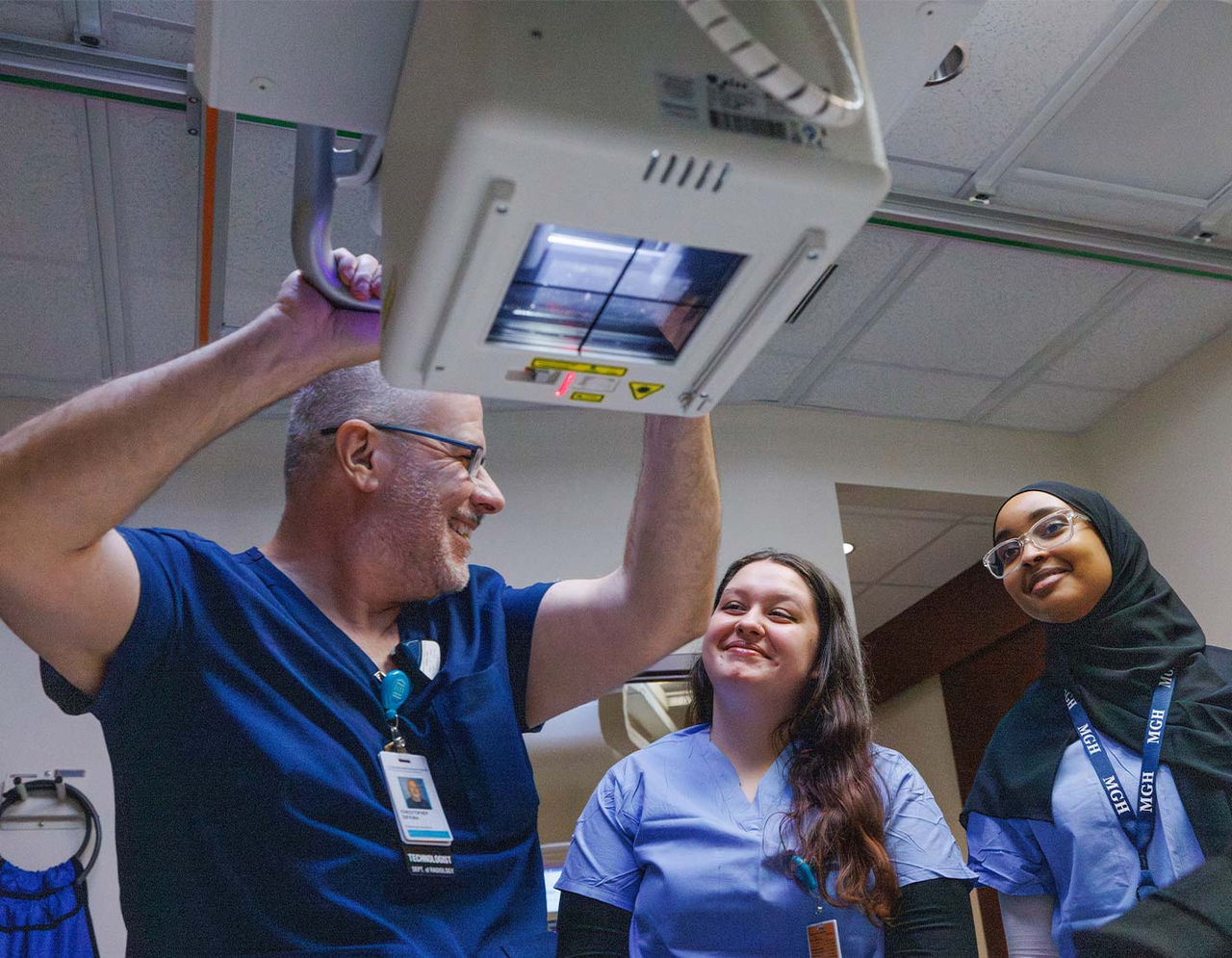 male technician holding medical equipment with his hand smiling next to two female students 