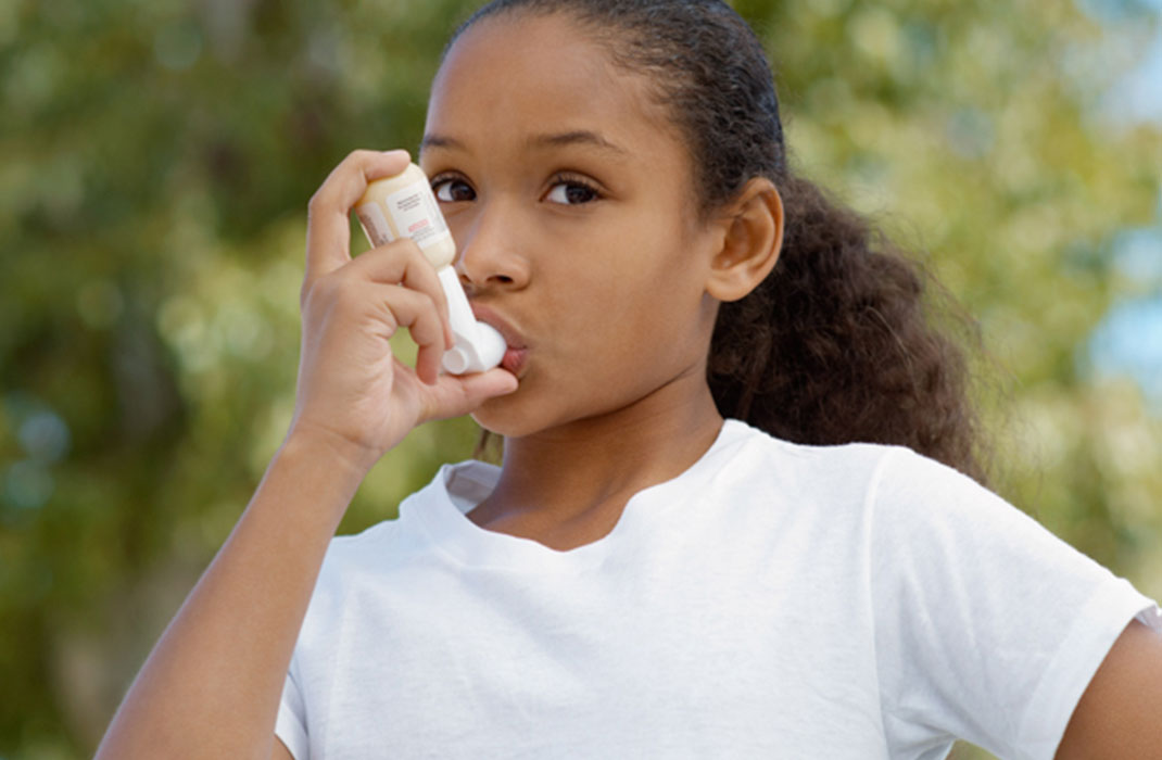 A girl uses an inhaler while outdoors.