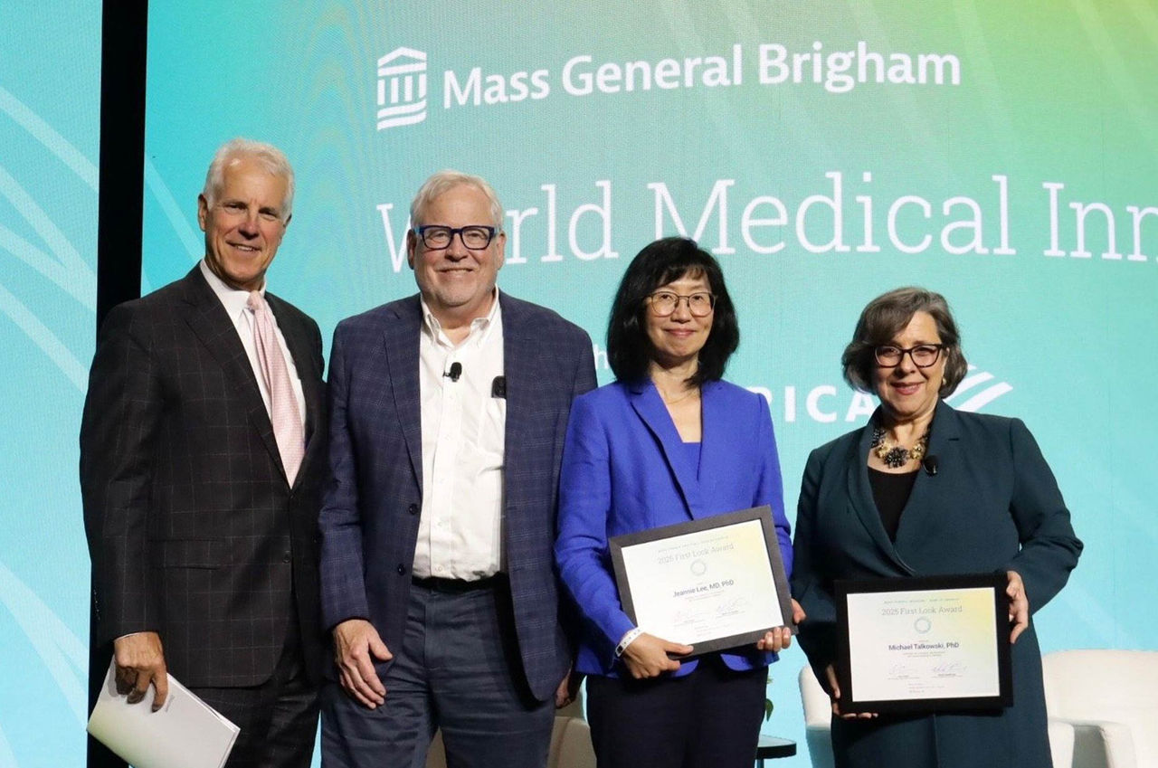 A group of individuals standing on stage during the Mass General Brigham World Medical Innovation Forum. Two people are holding framed certificates, while others are dressed in formal attire.