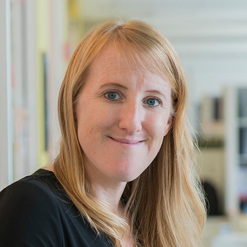 A woman with long blonde hair is seen in a modern office environment.