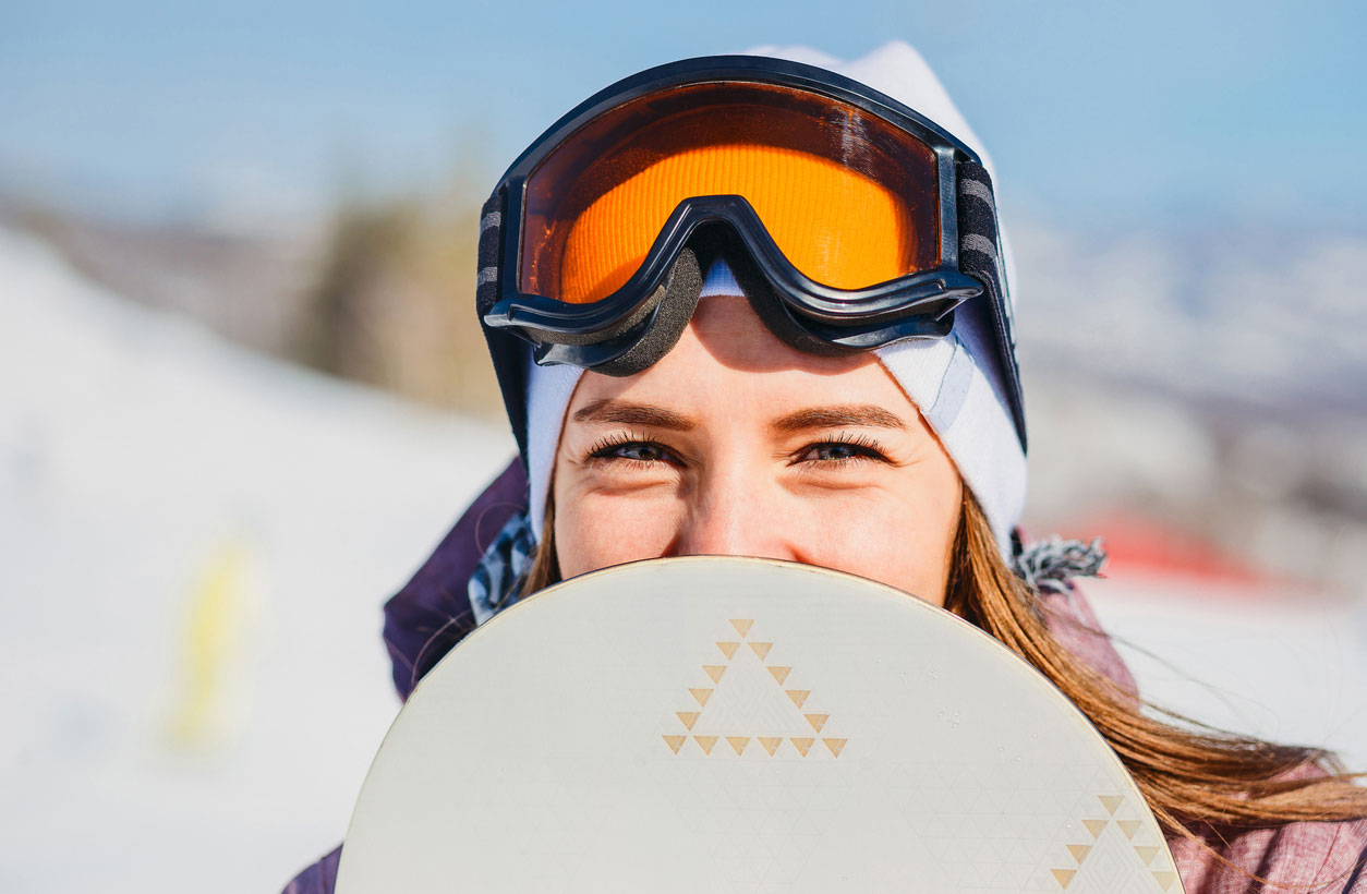 A young woman holding a snowboard and wearing protective gear.