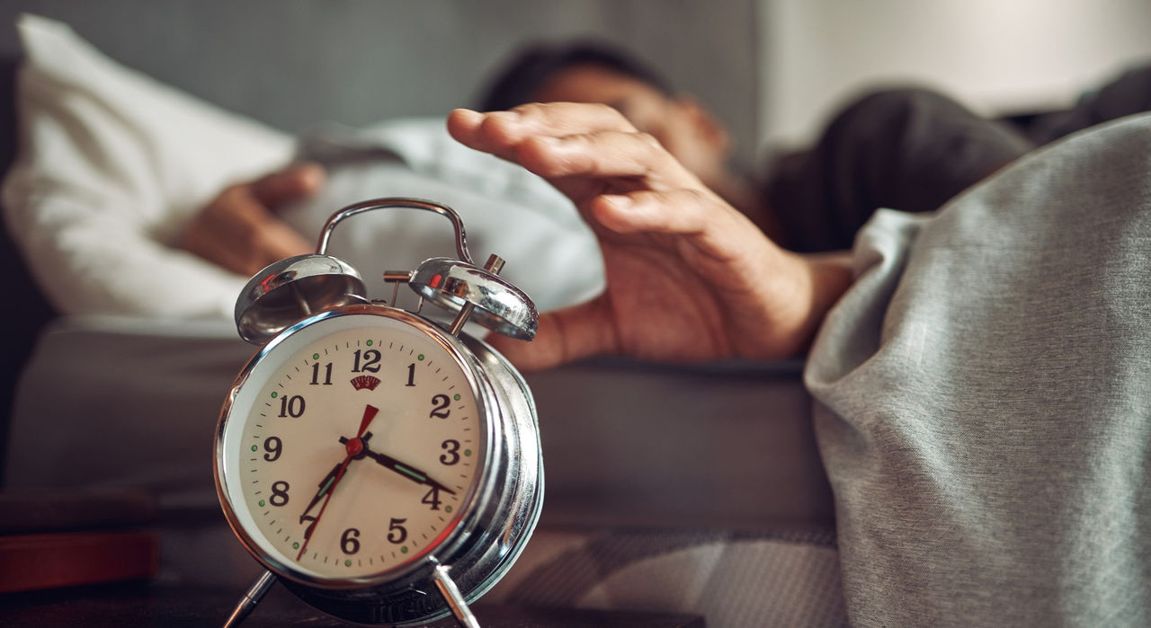 Man reaches for alarm clock on nightstand.