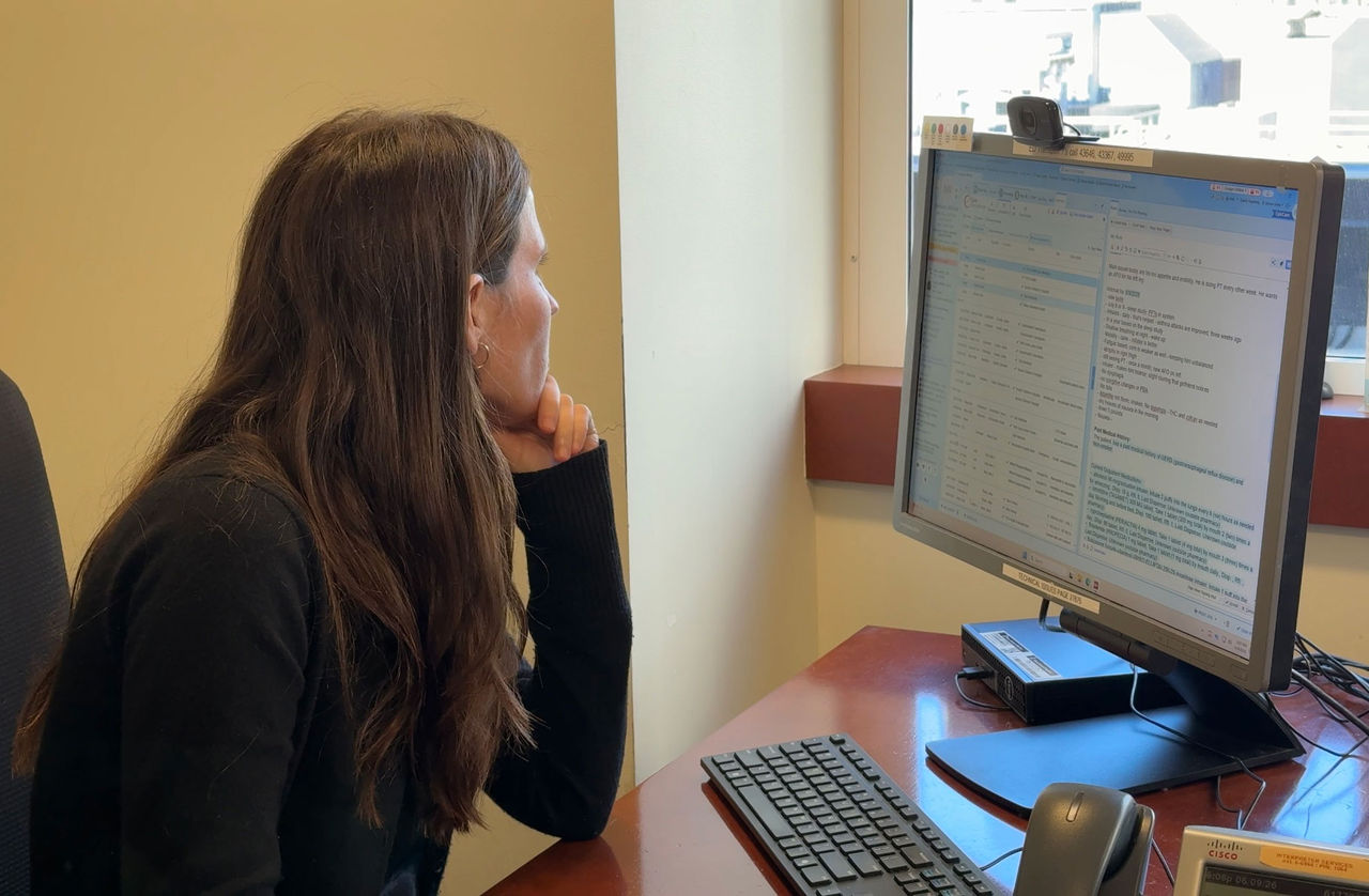 A woman sits at her desk and looks out her office window, away from her desk.