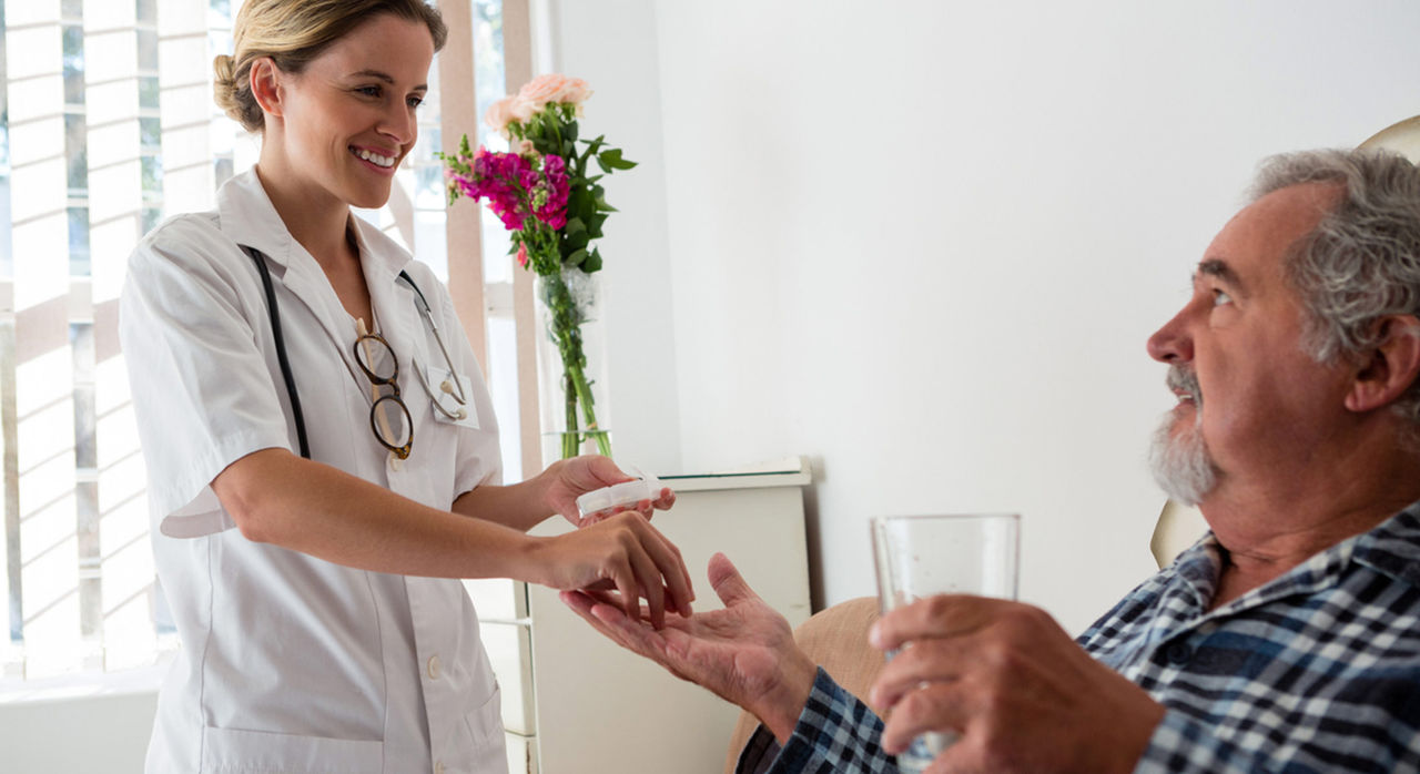 A doctor places medication in an older patient's hand as they get ready to take it with a glass of water
