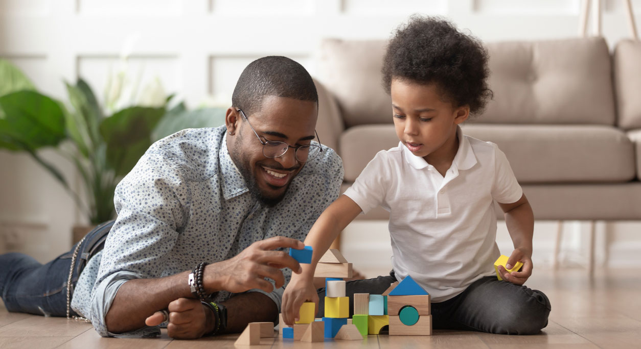 A father and son play with blocks at home.