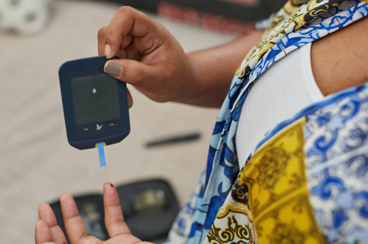 A person, with a drop of blood on their finger, gets ready to test their blood sugar level