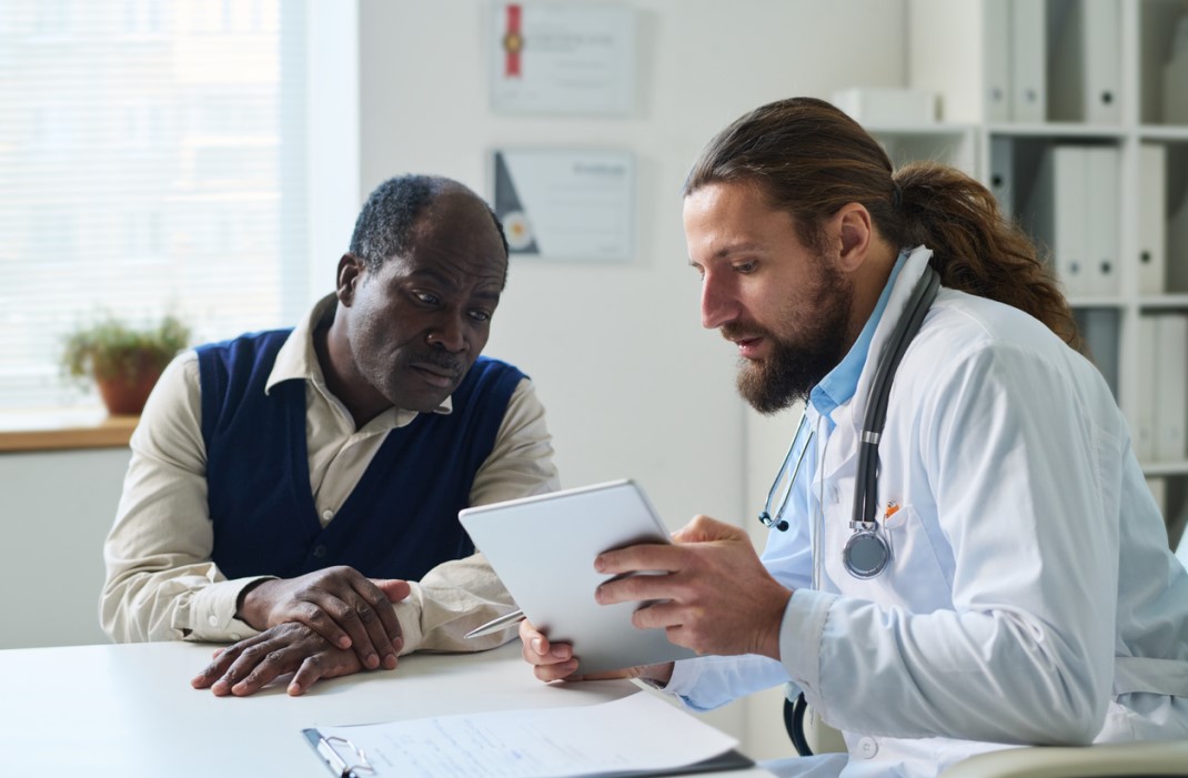 Older patient discusses bladder cancer care options with a doctor, reading from a tablet.