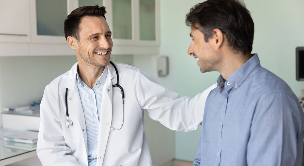 A cardiologist smiles at his patient and touches his shoulder.