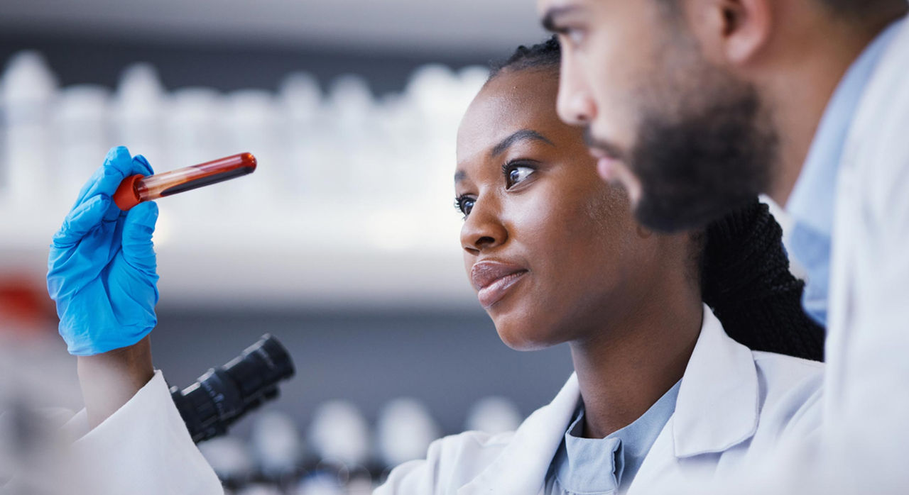 A researcher holds up a vial of blood in a lab for her and another researcher to study