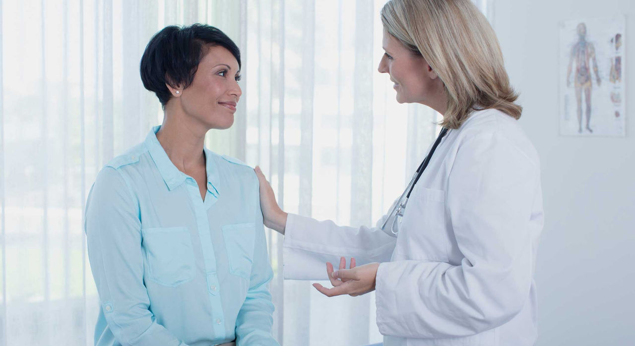 A supportive doctor talks with her female patient in the examination room.
