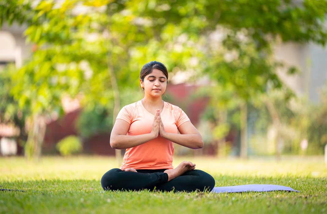 Woman in yoga pose meditating on the lawn.