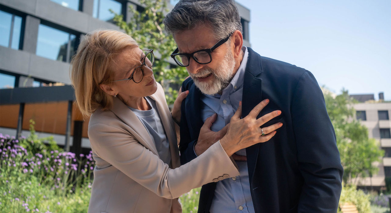 Senior man clutching his chest and looking faint while senior woman checks to see what is wrong