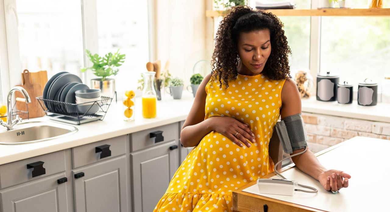 A pregnant woman checks her blood pressure at her kitchen island.