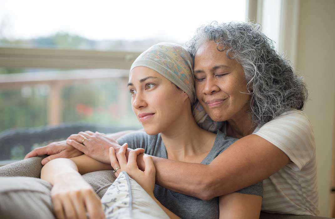 A mother embraces her young adult daughter, who wears a skull cap like a cancer patient.
