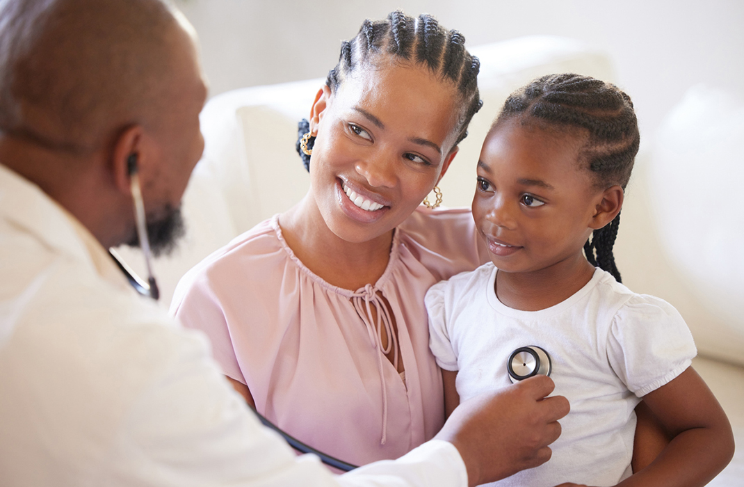 A mother holds her daughter as a pediatrician listens to the child’s breathing with a stethoscope, as part of treatment for cystic fibrosis. 