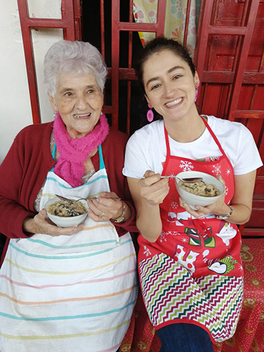 A mother and her adult daughter smile and hold their bowls of rice pudding