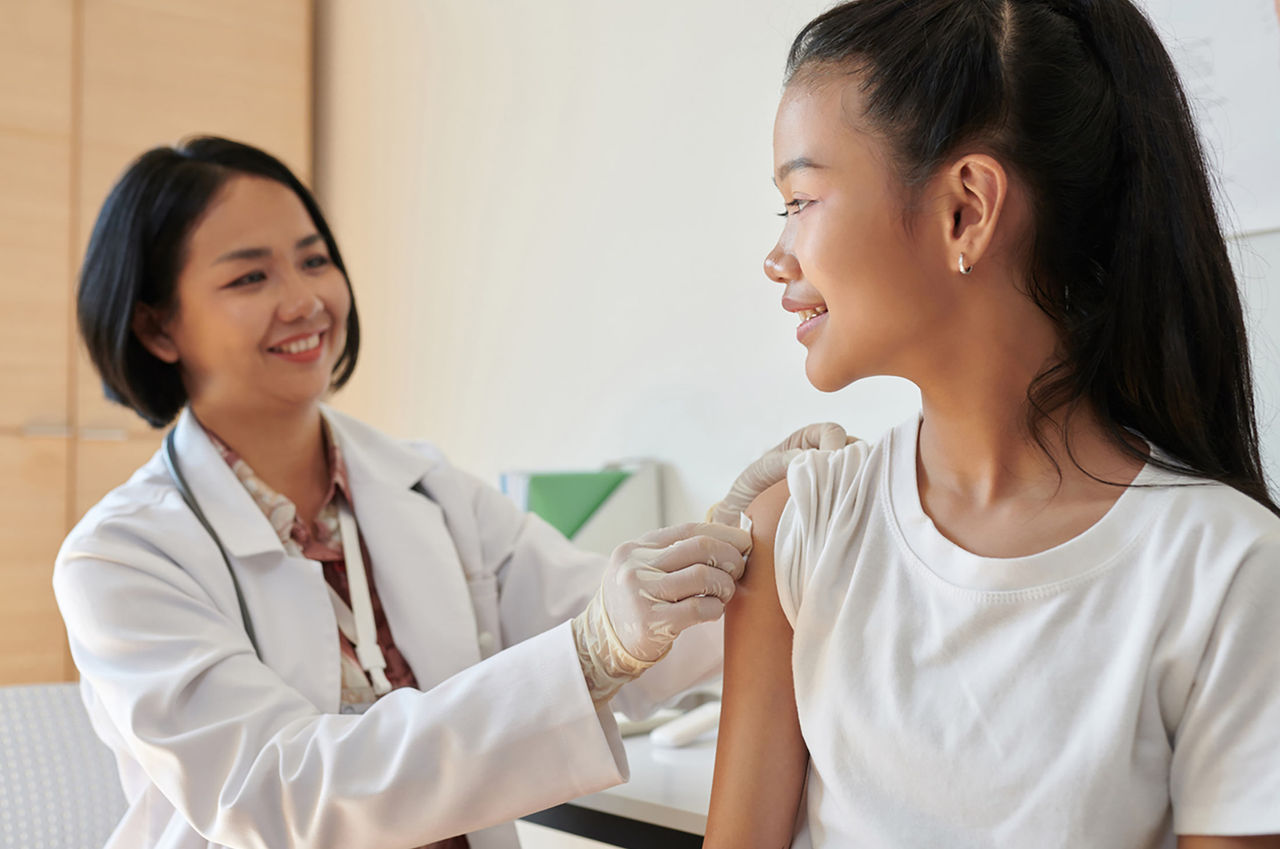 A smiling doctor prepares to give a preteen girl a vaccine