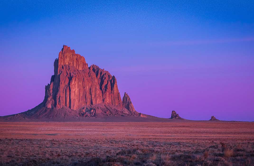 The Shiprock rock formation rises above the desert at sunrise.