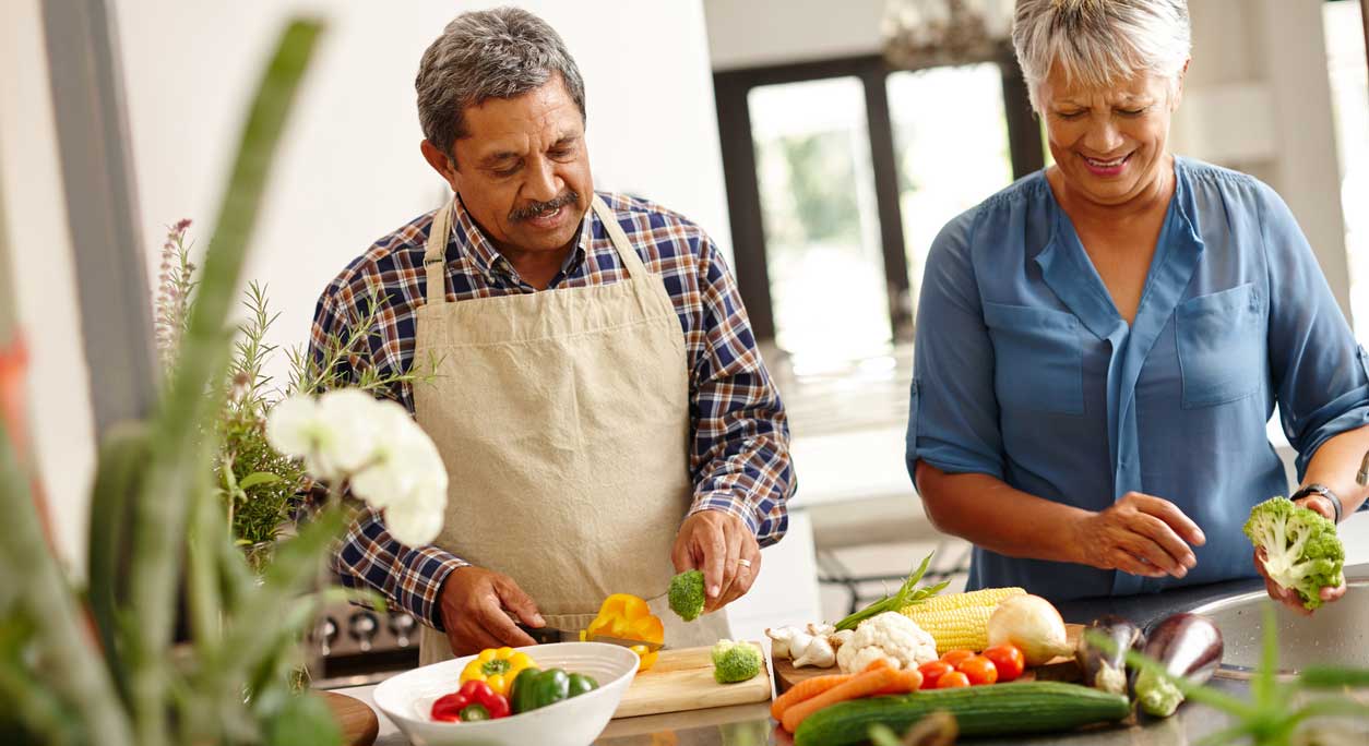 An older couple chops colorful vegetables together.