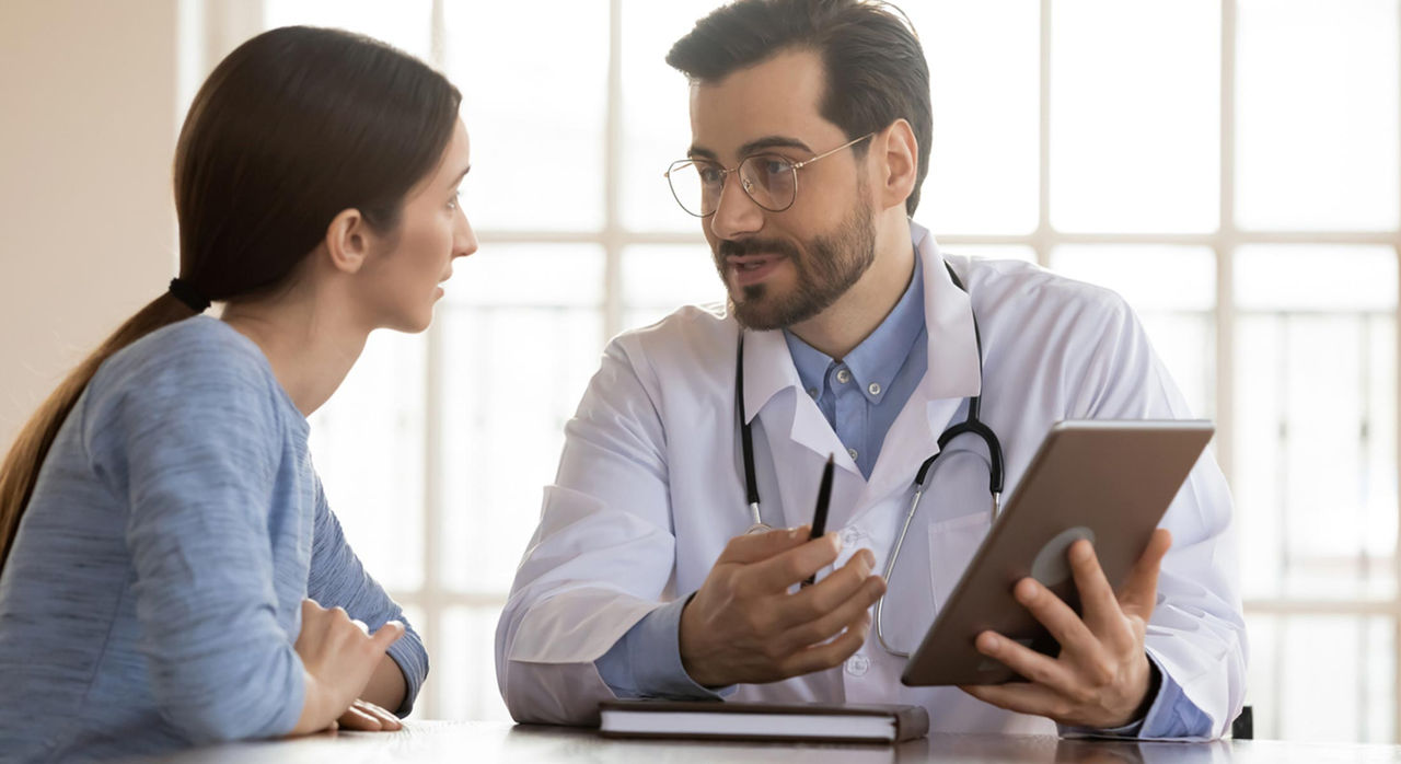 A doctor holds a tablet and explains some medical information to a patient.