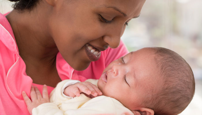 A smiling mother holds her sleeping baby.