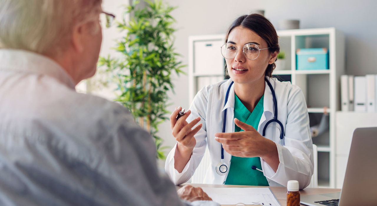 A doctor talks about early signs of Parkinson’s with an older patient at her desk.